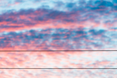 Blue and pink dramatic sunset clouds; 2 parallel telephone wires string across the width of the frame.