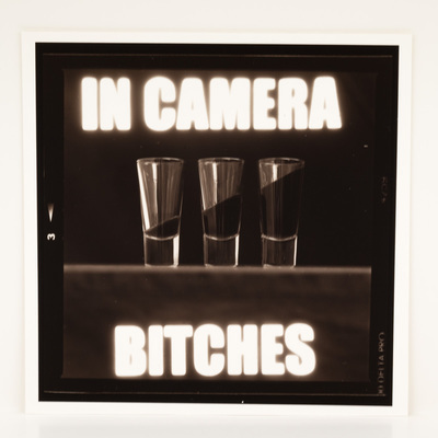 A frame of film, looking at three shot glasses with angled liquid in them. The title is overlaid in white macro text.