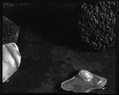 Closeup of 2 shell fragments, one with a pearl in it, and 2 bits of pumice on a dark background