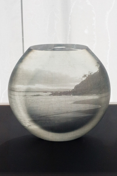 A round vase/bowl with a narrow hole. There is a seascape image on it.