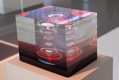 Rectangular cube with layers of red and clear glass. There are concentric circles in the layers.