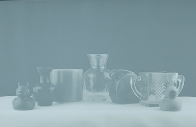 A hazy bluish black-and-white image with several glass items in a row. There is a rubber ducky on each end.