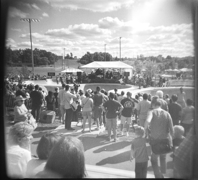 Overview of the show area, dozens of people watching the scene (their backs to the camera). A skater is riding the wall of the bowl.